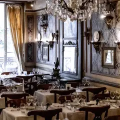 Tables dressées dans le plus vieux restaurant de Paris. Lustres en cristal, papier peint orné et vue sur la rue.