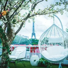 Un décor romantique pour un speed dating Paris, avec la Tour Eiffel en arrière-plan. Fauteuils blancs, balancelle et arbre fleuri créent une ambiance féerique.
