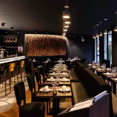Ambiance chic d'un restaurant avec un bar lumineux, des tables dressées et une décoration murale en bois. Un endroit parfait pour un dîner en tête-à-tête, un moom mam.