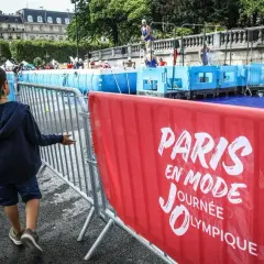 Un enfant observe une piscine temporaire installée pour une journée olympique à Paris. L'inscription "Paris en mode Journée Olympique" est visible sur une banderole rouge.