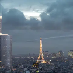 La Tour Montparnasse, en pleine rénovation, se dresse fièrement à Paris, illuminée par des faisceaux de lumière, dominant la ville et la Tour Eiffel scintillante.