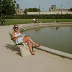Une femme lit au soleil, profitant d'un moment de détente pour ou bronzer à Paris, près d'un bassin.