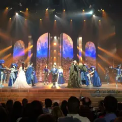 Scène du spectacle "Notre-Dame de Paris" avec des costumes d'époque et un décor évoquant la ville.
