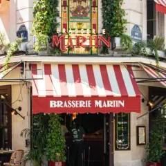 La Brasserie Martin, un coin parisien charmant avec ses auvents rayés rouges et blancs, ses plantes grimpantes et son enseigne lumineuse.