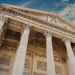 Le **Panthéon de Paris**, majestueux avec ses colonnes imposantes et ses bas-reliefs, se dresse sous un ciel bleu nuageux.