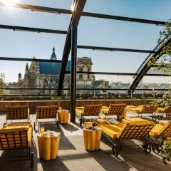 Profitez d'un brunch rooftop à Paris avec vue sur les toits et une église majestueuse. Des chaises longues jaunes invitent à la détente.