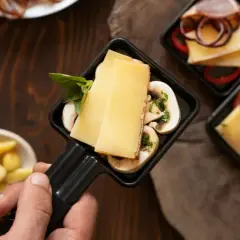 Poignée de raclette avec fromage, champignons et basilic, prêt pour un dîner dans un restaurant raclette Paris.