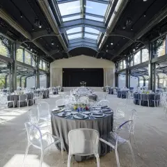 Salle de réception lumineuse au pavillon Gabriel, tables rondes dressées sous une verrière, chaises transparentes.