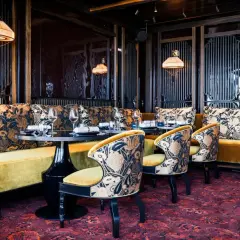 Ambiance luxueuse d'un restaurant à mun paris. Banquettes velours ocre, coussins fleuris, chaises élégantes et tapis persan.