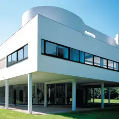 La Villa Savoye, icône de l'architecture moderne, se dresse sur pilotis dans un écrin de verdure, sous un ciel bleu éclatant.
