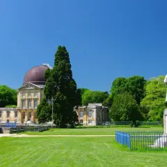 Un grand bâtiment avec un dôme rouge, entouré d'arbres verts et d'une pelouse. Une statue se dresse devant, comme si elle surveillait le hangar Y.