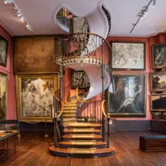 Escalier en colimaçon majestueux au cœur d'un musée insolite à Paris, entouré de tableaux sombres et évocateurs.