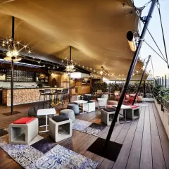 Ambiance chaleureuse sur un rooftop Paris pas cher, avec bar en bois, lumières scintillantes et mobilier cosy. Idéal pour un moment détente.