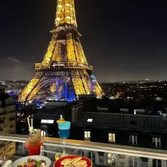 Vue nocturne de Paris depuis un balcon avec des cocktails et des tapas, la Tour Eiffel illuminée en arrière-plan. C'est le 10ème ciel !