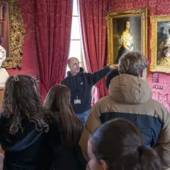 Visite guidée dans la Maison de Victor Hugo à Paris. Un guide montre des tableaux et un buste de l'écrivain à un groupe de visiteurs.
