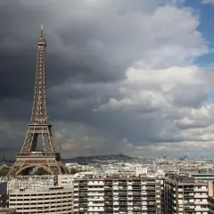 La Tour Eiffel, une des célèbres structures conçues par Gustave Eiffel, se dresse fièrement au-dessus de Paris sous un ciel orageux et lumineux.