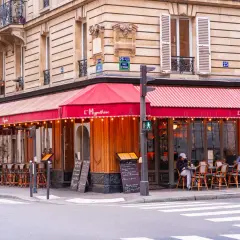 Un café parisien avec des tables en terrasse sous un auvent rouge. L'ambiance d'un food court à Paris.