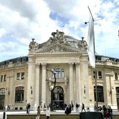 Le musée de la Bourse, un bâtiment majestueux, accueille des visiteurs sous un ciel nuageux. Une sculpture d'arbre intrigante se dresse devant l'entrée.