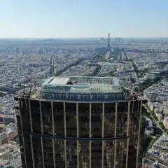 Vue aérienne de la **Tour Montparnasse** avec sa terrasse panoramique. Paris s'étend à perte de vue, avec la Tour Eiffel au loin.
