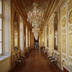 Un long couloir orné de dorures et de lustres étincelants, rappelant la splendeur du **hôtel de la Marine**.