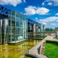 Le bâtiment moderne de la Cité des sciences Paris, avec ses structures en verre et en métal, reflète le ciel bleu et les nuages.