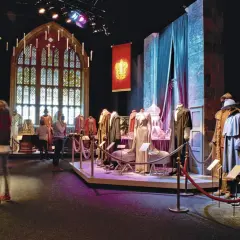 Costumes et artefacts de l'exposition Harry Potter, avec des bannières de Poudlard et une grande fenêtre gothique.