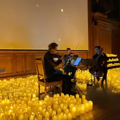 Un trio de musiciens joue dans une salle baignée par la douce lueur de milliers de bougies. Un concert à la bougie magique.