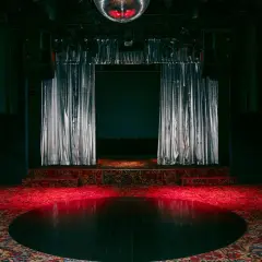 Scène de concert avec rideaux argentés, tapis persan et boule disco rougeoyante, évoquant l'ambiance d'un bus palladium.