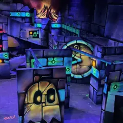 Labyrinthe de laser game aux couleurs vives, avec des fantômes et un volcan en arrière-plan. Le panneau "LA TÊTE DANS LES NUAGES" suggère une expérience amusante.