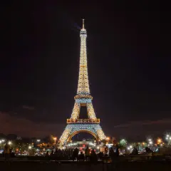 La Tour Eiffel illuminée la nuit, un spectacle magique avec des faisceaux de lumière traversant le ciel parisien.