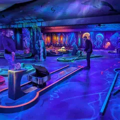 Ambiance sous-marine pour un escape game avec enfant. Parcours de mini-golf fluorescent, décoré de méduses et de dauphins, promettant une aventure ludique.