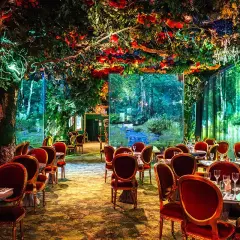 Un restaurant gastronomique féerique, avec des tables dressées sous une voûte de verdure luxuriante et des décors de forêt enchantée.