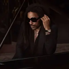 Lenny Kravitz, élégant à Paris, pose près d'un piano, lunettes noires et chaîne argentée.