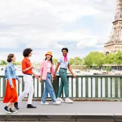 Quatre amis profitent d'une visite insolite Paris gratuit, traversant un pont avec la Tour Eiffel en arrière-plan.