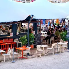 Bar animé sur les quais parisiens, avec des tables et des chaises en terrasse sous une grande tente blanche.