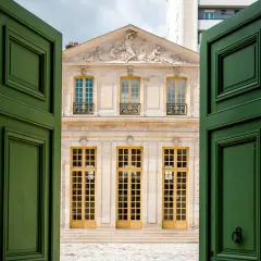 Portes vertes ouvertes sur le pavillon Vendôme à Paris, avec sa façade ornée et ses grandes fenêtres jaunes.