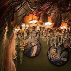Décor luxuriant et excentrique d'un restaurant insolite à Paris, avec des lustres ornés, des plantes suspendues et des tableaux d'oiseaux exotiques.