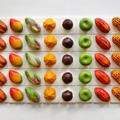 Assortiment de chocolats aux formes fruitées et originales, rappelant l'univers de Cédric Grolet. Des mangues, citrons, cacahués, fèves de cacao et autres délices.