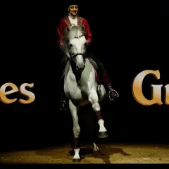 Une écuyère en tenue rouge sublime un cheval blanc lors d'un spectacle des Folies Gruss.