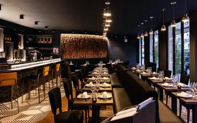 Ambiance chic d'un restaurant avec un bar lumineux, des tables dressées et une décoration murale en bois. Un endroit parfait pour un dîner en tête-à-tête, un moom mam.