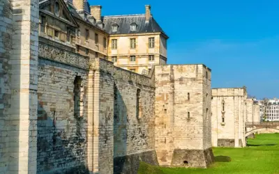 Murs imposants et tours de pierre du **château de Vincennes** sous un ciel bleu éclatant, avec des bâtiments historiques en arrière-plan.