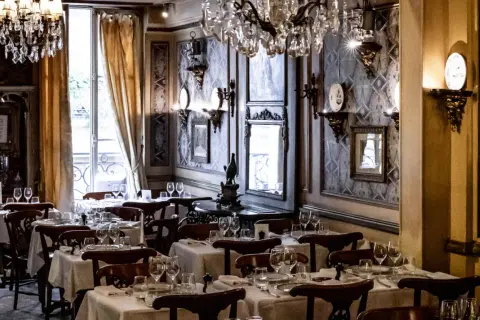 Tables dressées dans le plus vieux restaurant de Paris. Lustres en cristal, papier peint orné et vue sur la rue.