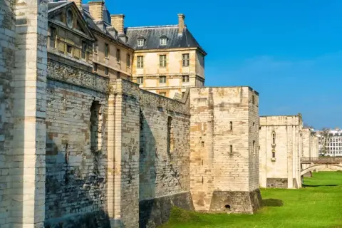 Murs imposants et tours de pierre du **château de Vincennes** sous un ciel bleu éclatant, avec des bâtiments historiques en arrière-plan.