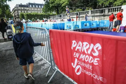 Un enfant observe une piscine temporaire installée pour une journée olympique à Paris. L'inscription "Paris en mode Journée Olympique" est visible sur une banderole rouge.