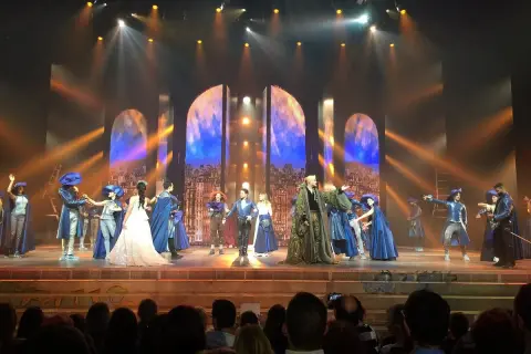 Scène du spectacle "Notre-Dame de Paris" avec des costumes d'époque et un décor évoquant la ville.