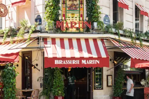 La Brasserie Martin, un coin parisien charmant avec ses auvents rayés rouges et blancs, ses plantes grimpantes et son enseigne lumineuse.