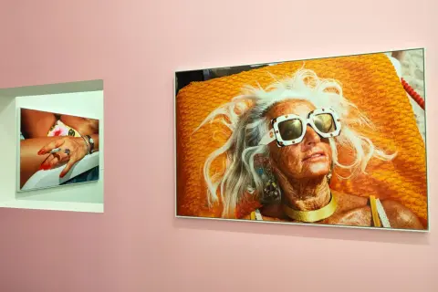 Une femme âgée aux cheveux blancs et lunettes de soleil extravagantes, sur une serviette orange vif. Une autre photo montre une main manucurée tenant une cigarette. Martin Parr expo.