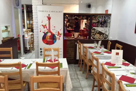 Tables dressées dans un restaurant portugais. Un homme derrière le bar, une guitare colorée sur une bannière.