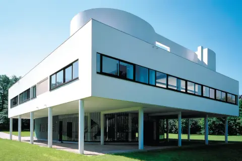 La Villa Savoye, icône de l'architecture moderne, se dresse sur pilotis dans un écrin de verdure, sous un ciel bleu éclatant.