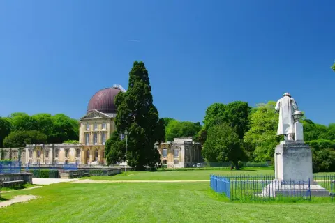 Un grand bâtiment avec un dôme rouge, entouré d'arbres verts et d'une pelouse. Une statue se dresse devant, comme si elle surveillait le hangar Y.